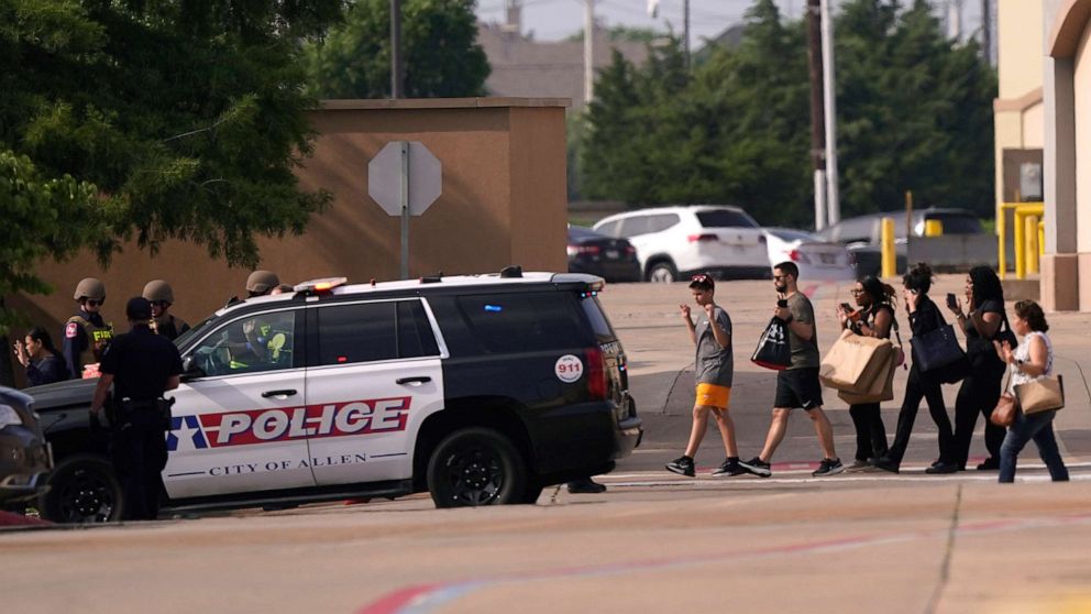 People raise their hands as they leave a shopping center after a shooting, May 6, 2023, in Allen, Texas.